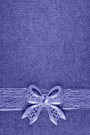 Elegant shiny tied glittering bow and ribbon on natural burlap textile. Image toned in very peri, color of year 2022. Vertical background with Christmas decor and large copy space. View from above.の写真素材
