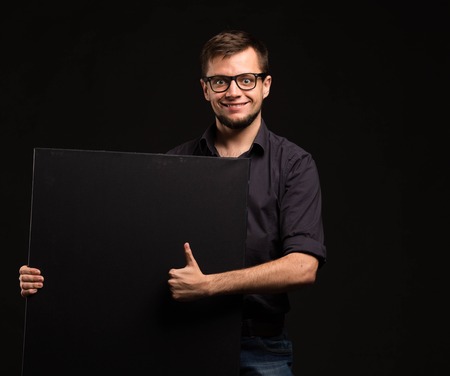 Young happy man portrait of a confident businessman showing presentation, pointing paper placard black background. Ideal for banners, registration forms, presentation, landings, presenting concept.の写真素材