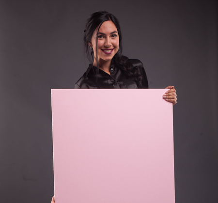 Young happy woman portrait of a confident businesswoman showing presentation, pointing placard black background. Ideal for banners, registration forms, presentation, landings, presenting concept.の写真素材