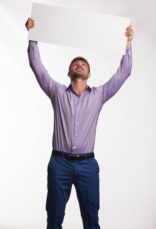 Young pry man portrait of a confident businessman showing presentation, pointing paper placard gray background. Ideal for banners, registration forms, presentation, landings, presenting concept.の写真素材