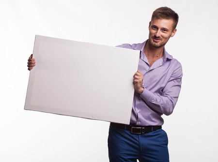 Young glad man portrait of a confident businessman showing presentation, pointing paper placard gray background. Ideal for banners, registration forms, presentation, landings, presenting concept.の写真素材