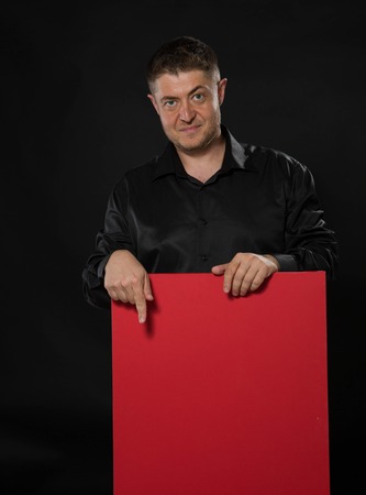 Young confident man portrait of a confident businessman showing presentation, pointing placard black background. Ideal for banners, registration forms, presentation, landings, presenting concept.の写真素材