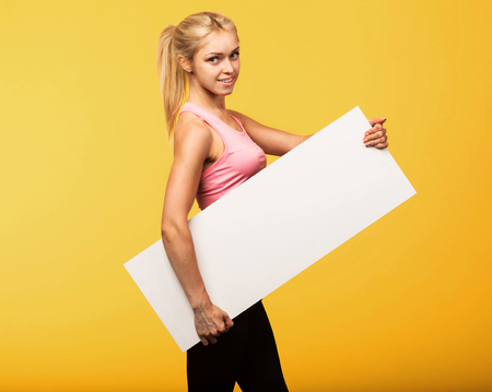 Young happy woman portrait of a confident businesswoman showing presentation, pointing placard yellow background. Ideal for banners, registration forms, presentation, landings, presenting concept.の写真素材