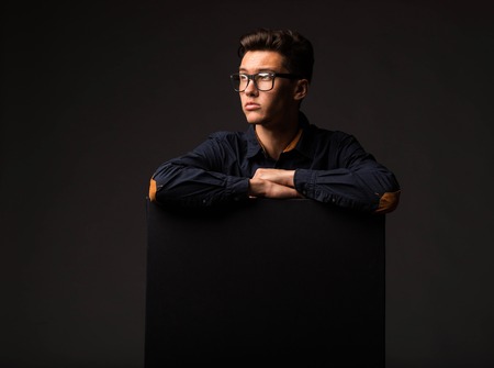 Young pensive man portrait of a confident businessman showing presentation, pointing paper placard black background. Ideal for banners, registration forms, presentation, landings, presenting concept.の写真素材