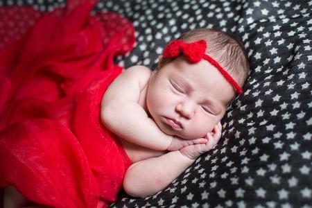 Sleeping pretty newborn in red dress and a small ribbon on his head.の写真素材