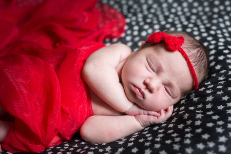 Sleeping pretty newborn in red dress and a small ribbon on his head.の写真素材