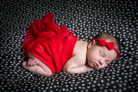 Sleeping pretty newborn in red dress and a small ribbon on his head.の写真素材