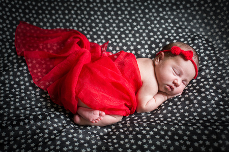 Sleeping pretty newborn in red dress and a small ribbon on his head.の写真素材