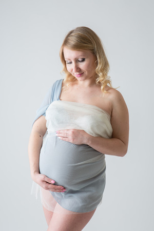 Happy pregnant young woman in love on the background. Hands on the tummy. Young mom tenderly stroked pregnant belly with unborn baby.の写真素材