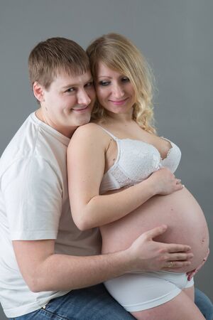 Beautiful pregnant couple in love on the background.Hands of husband on the tummy of his pregnant wife. Young man tenderly stroked pregnant belly of his wife. Husband kissing pregnant belly.の写真素材