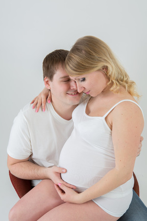 Beautiful pregnant couple in love on the background.Hands of husband on the tummy of his pregnant wife. Young man tenderly stroked pregnant belly of his wife. Husband kissing pregnant belly.の写真素材