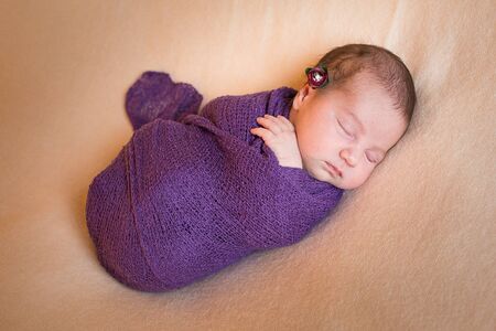 Sleeping newborn baby girl in a violet knit baby blanket. Isolated on background.の写真素材