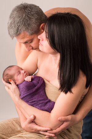 Happy family couple in love on the background. Portrait of happy young family tenderly keeping their sleeping baby on gray background.の写真素材