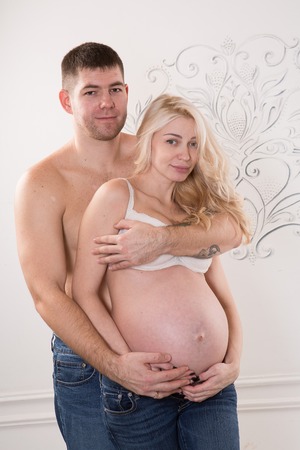 Beautiful pregnant couple in love on the background. Hands of husband on the tummy of his pregnant wife. Young man tenderly stroked pregnant belly of his wife. Husband kissing pregnant belly.の写真素材