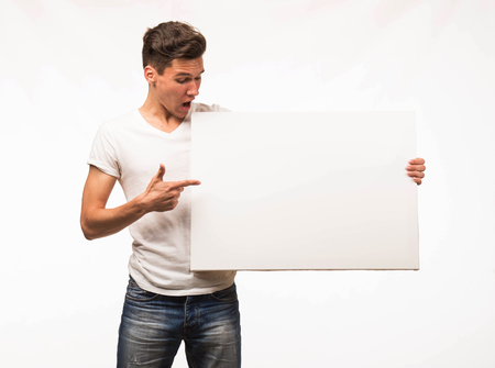 Young surprised man portrait of a confident businessman showing presentation, pointing paper placard gray background. Ideal for banners, registration forms, presentation, landings, presenting concept.の写真素材