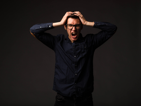 Young angry man portrait of a confident businessman showing by hands on a black background. Ideal...