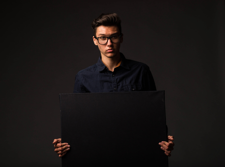 Young confident man portrait of a businessman showing presentation, pointing paper placard black background. Ideal for banners, registration forms, presentation, landings, presenting concept.の写真素材