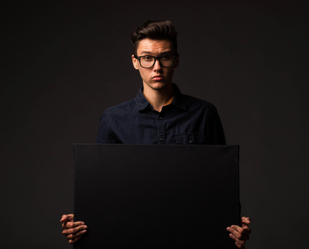 Young confident man portrait of a businessman showing presentation, pointing paper placard black background. Ideal for banners, registration forms, presentation, landings, presenting concept.の写真素材