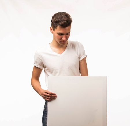 Young wistful man portrait of a confident businessman showing presentation, pointing paper placard gray background. Ideal for banners, registration forms, presentation, landings, presenting concept.の写真素材