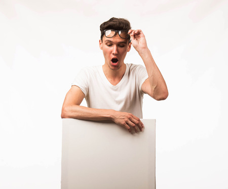 Young surprised man portrait of a confident businessman showing presentation, pointing paper placard gray background. Ideal for banners, registration forms, presentation, landings, presenting concept.の写真素材