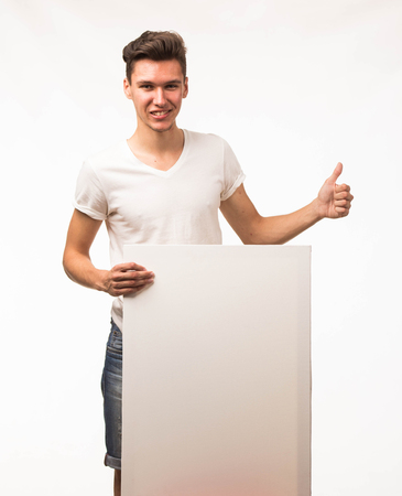 Young happy man portrait of a confident businessman showing presentation, pointing paper placard gray background. Ideal for banners, registration forms, presentation, landings, presenting concept.の写真素材