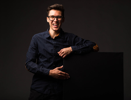 Young happy man portrait of a confident businessman showing presentation, pointing paper placard black background. Ideal for banners, registration forms, presentation, landings, presenting concept.の写真素材