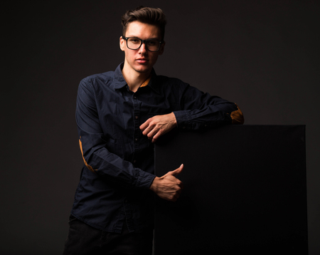 Young sexy man portrait of a confident businessman showing presentation, pointing paper placard black background.の写真素材