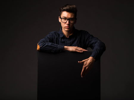 Young serious man portrait of a confident businessman showing presentation, pointing paper placard black background. Ideal for banners, registration forms, presentation, landings, presenting concept.の写真素材