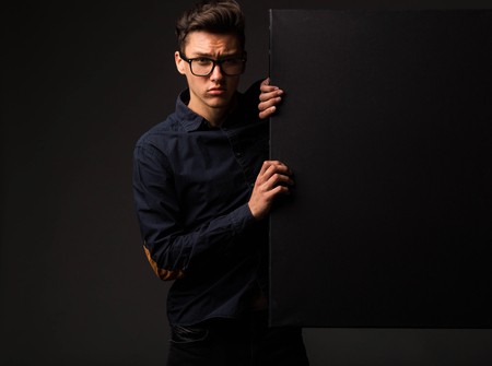 Young pensive man portrait of a confident businessman showing presentation, pointing paper placard black background. Ideal for banners, registration forms, presentation, landings, presenting concept.の写真素材