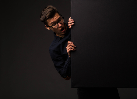 Young surprised man portrait of a confident businessman showing presentation, pointing placard black background. Ideal for banners, registration forms, presentation, landings, presenting concept.の写真素材