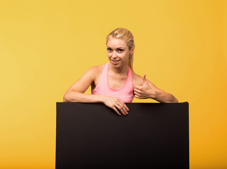 Young cheerful portrait of a confident woman showing presentation, pointing placard yellow background.の写真素材
