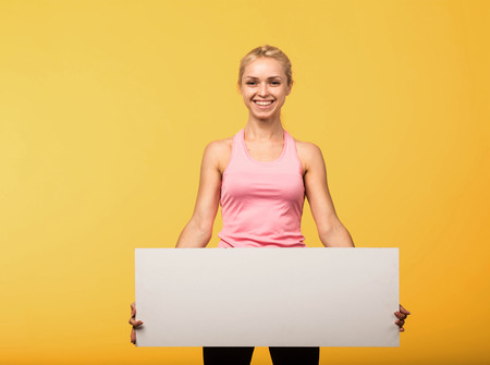 Young glad woman portrait of a confident businesswoman showing presentation, pointing placard yellow background. Ideal for banners, registration forms, presentation, landings, presenting concept.の写真素材