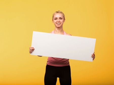 Young glad woman portrait of a confident businesswoman showing presentation, pointing placard yellow background. Ideal for banners, registration forms, presentation, landings, presenting concept.の写真素材