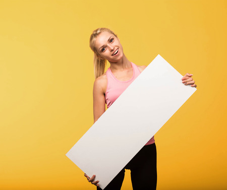 Young glad portrait of a confident woman showing presentation, pointing placard yellow background.の写真素材