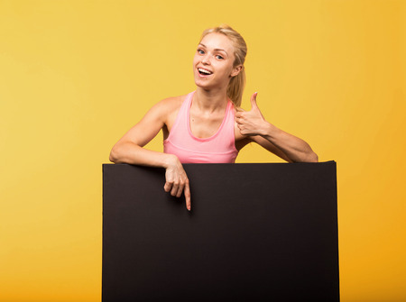 Young happy portrait of a confident woman showing presentation, pointing placard yellow background.の写真素材