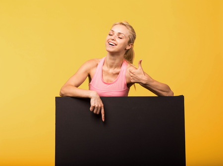 Young happy woman portrait of a confident businesswoman showing presentation, pointing placard yellow background. Ideal for banners, registration forms, presentation, landings, presenting concept.の写真素材