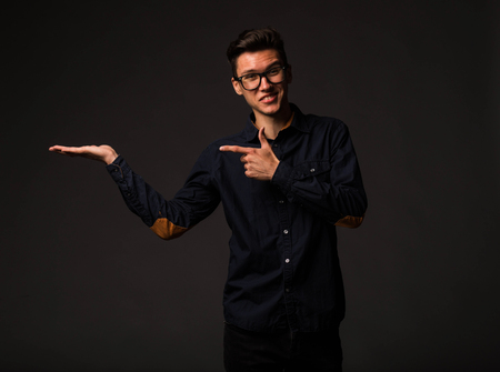 Young jocular man portrait of a confident businessman showing by hands on a black background. Ideal for banners, registration forms, presentation, landings, presenting concept.の写真素材