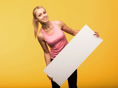 Young glad portrait of a confident woman showing presentation, pointing placard yellow background. Ideal for banners, registration forms, presentation, landings, presenting concept.の写真素材