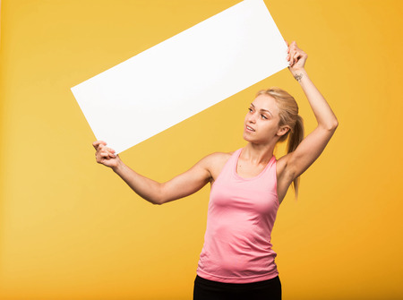 Young pry portrait of a confident woman showing presentation, pointing placard yellow background. Ideal for banners, registration forms, presentation, landings, presenting concept.の写真素材