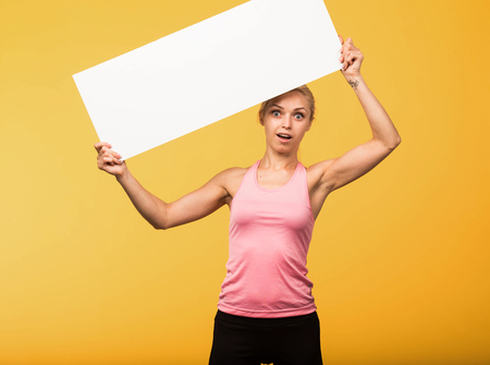 Young surprised portrait of a confident woman showing presentation, pointing placard yellow background. Ideal for banners, registration forms, presentation, landings, presenting concept.の写真素材
