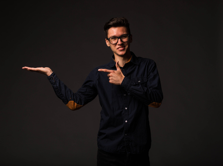 Young jocular man portrait of a confident businessman showing by hands on a black background. Ideal for banners, registration forms, presentation, landings, presenting concept.の写真素材