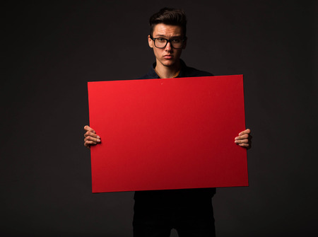Young serious man portrait of a confident businessman showing presentation, pointing paper placard black background. Ideal for banners, registration forms, presentation, landings, presenting concept.の写真素材
