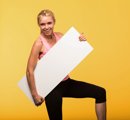 Young cheerful portrait of a confident woman showing presentation, pointing placard yellow background. Ideal for banners, registration forms, presentation, landings, presenting concept.の写真素材