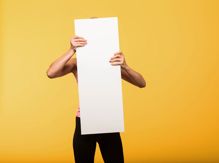 Young playful portrait of a confident woman showing presentation, pointing placard yellow background. Ideal for banners, registration forms, presentation, landings, presenting concept.の写真素材