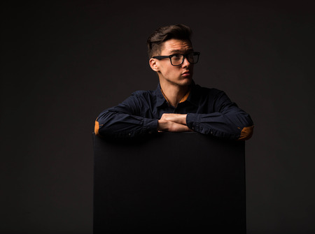 Young wistful man portrait of a confident businessman showing presentation, pointing paper placard black background. Ideal for banners, registration forms, presentation, landings, presenting concept.の写真素材
