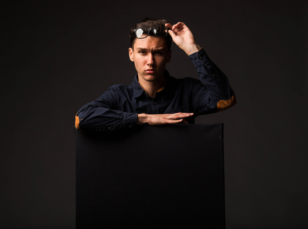 Young wistful man portrait of a confident businessman showing presentation, pointing paper placard black background. Ideal for banners, registration forms, presentation, landings, presenting concept.の写真素材