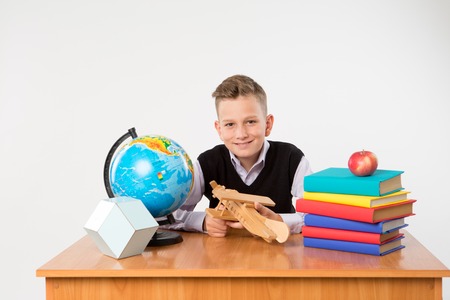 Cute schoolboy sit at a school desk isolated on white background. Ideal for banners, registration forms, presentation.の写真素材