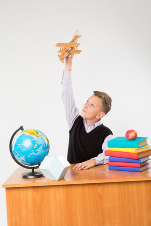 Cute schoolboy plays by airplane at a school desk isolated on white background. Ideal for banners, registration forms, presentation, school concept.の写真素材