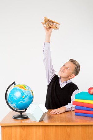 Cute schoolboy plays by airplane at a school desk isolated on white background. Ideal for banners, registration forms, presentation, school concept.の写真素材