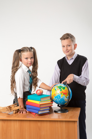 Happy boy and girl sit at a school desk, isolated on white background. Ideal for banners, registration forms, presentation, landings, presenting concept.の写真素材